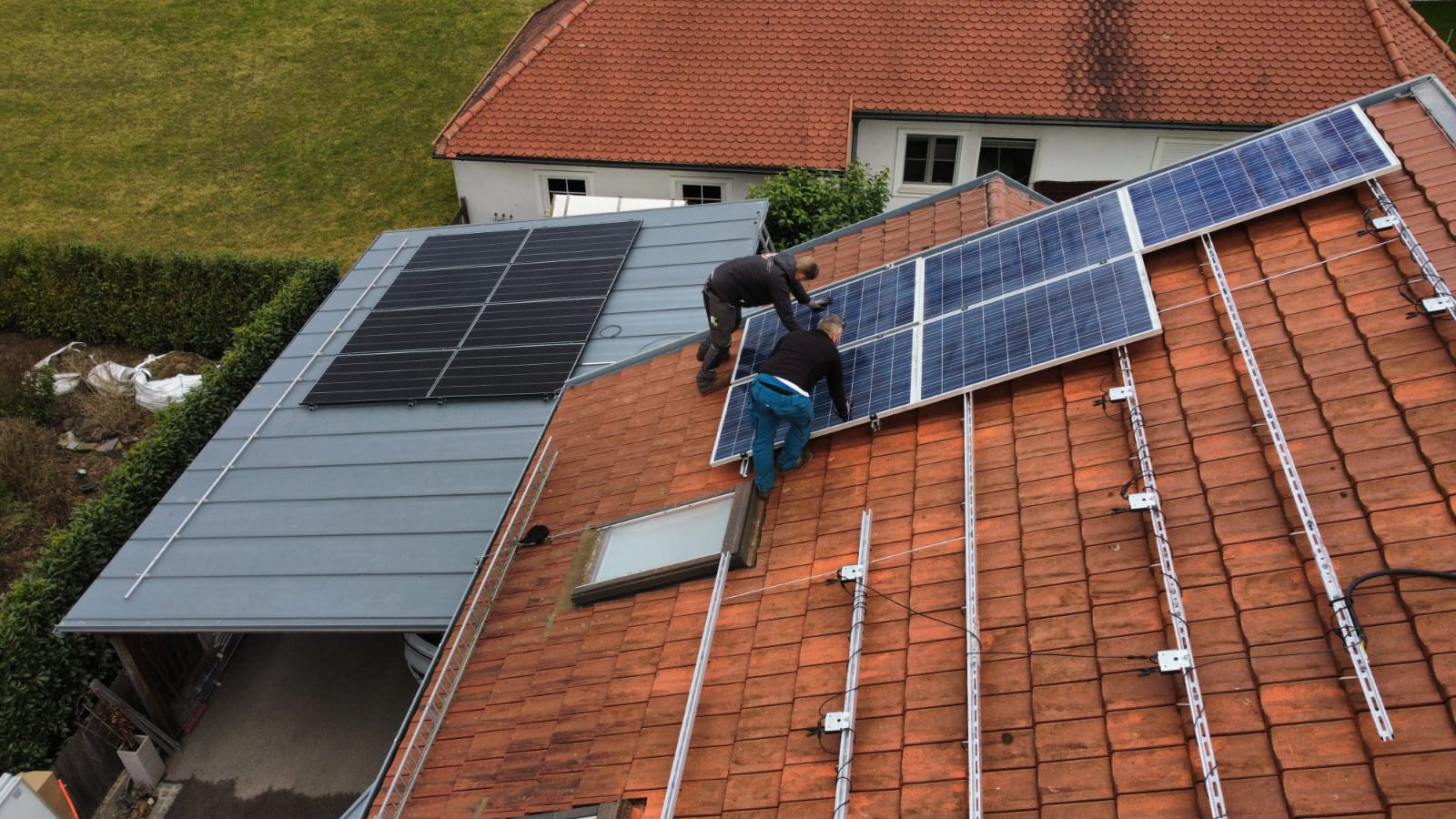 Arbeiter bauen Solaranlage auf dem Dach eines Hauses. Männertechniker in Helmen tragen Photovoltaik-Solarmodule im Freien.